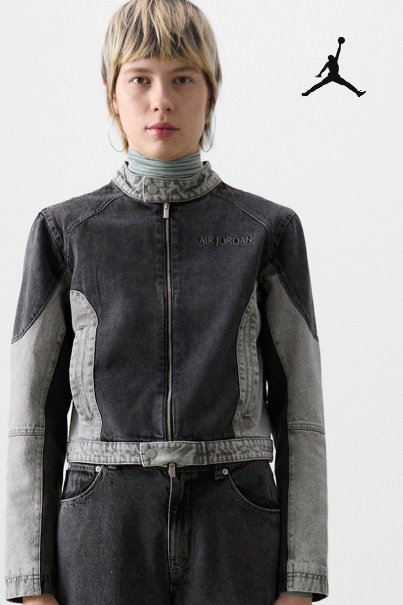 Una persona con pelo corto y claro lleva una chaqueta de mezclilla con cierre, en un diseño de bloques de color, que presenta la marca "Air Jordan", sobre un fondo gris.