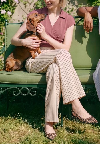 Donna seduta su una panchina verde all'aperto, tiene in grembo un piccolo bassotto marrone, sorride e accarezza il cane.