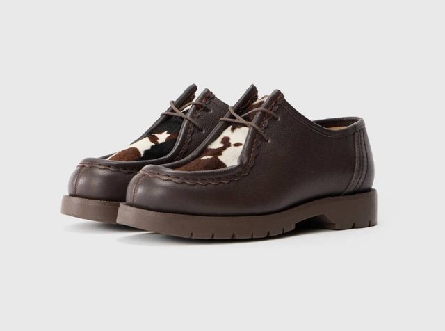 Sapatos de couro castanho com bico arredondado, apresentando detalhes em couro de vaca em castanho e branco, costuras decorativas e uma sola de borracha texturizada.