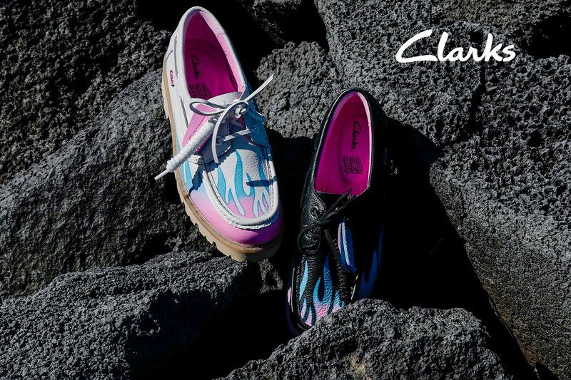 Zwei bunte Clarks-Schuhe mit Flammenmustern, einer in Pink und Weiß, einer in Schwarz und Blau, platziert auf rauen vulkanischen Felsen.
