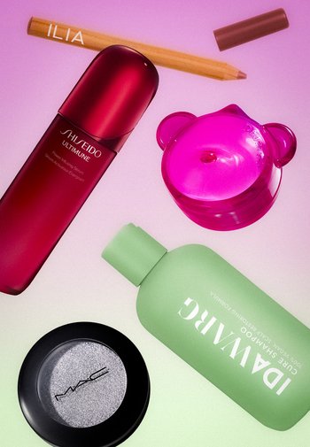 Bouteille de sérum Shiseido rouge, shampoing Idawarg vert, fard à paupières MAC argenté, contenant en forme d'ours rose et crayon ILIA en bois sur fond rose.