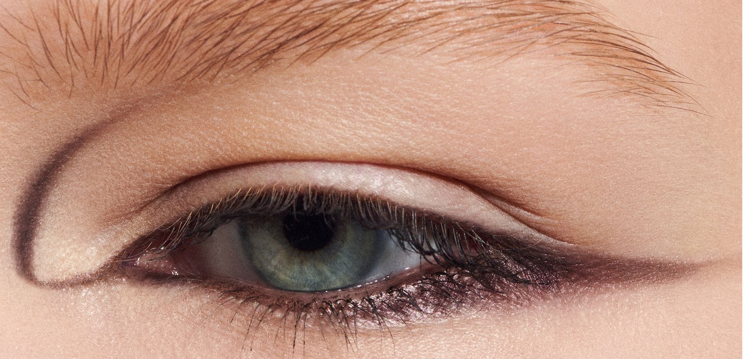 Gros plan sur un œil avec une paupière douce et neutre et un eyeliner ailé audacieux et sombre. L'iris est verdâtre avec une apparence texturée.