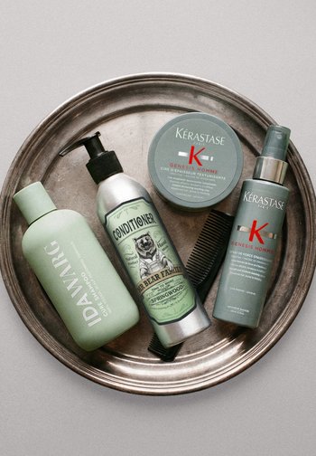 Rund metalbakke med fire hårplejeprodukter og en sort kam arrangeret pænt på en lys baggrund.