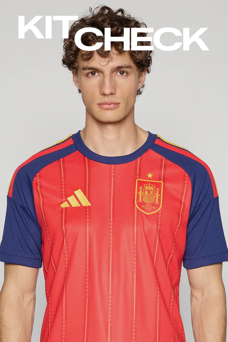 Tânăr cu păr creț purtând tricoul de fotbal al Spaniei roșu și albastru cu sigla și emblema Adidas, textul "KIT CHECK" deasupra.