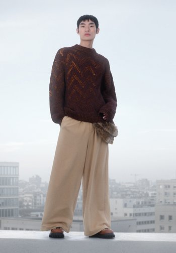 Pull en tricot texturé marron avec un motif en chevrons, pantalon large beige décontracté, et chaussures foncées avec une sangle à motif.