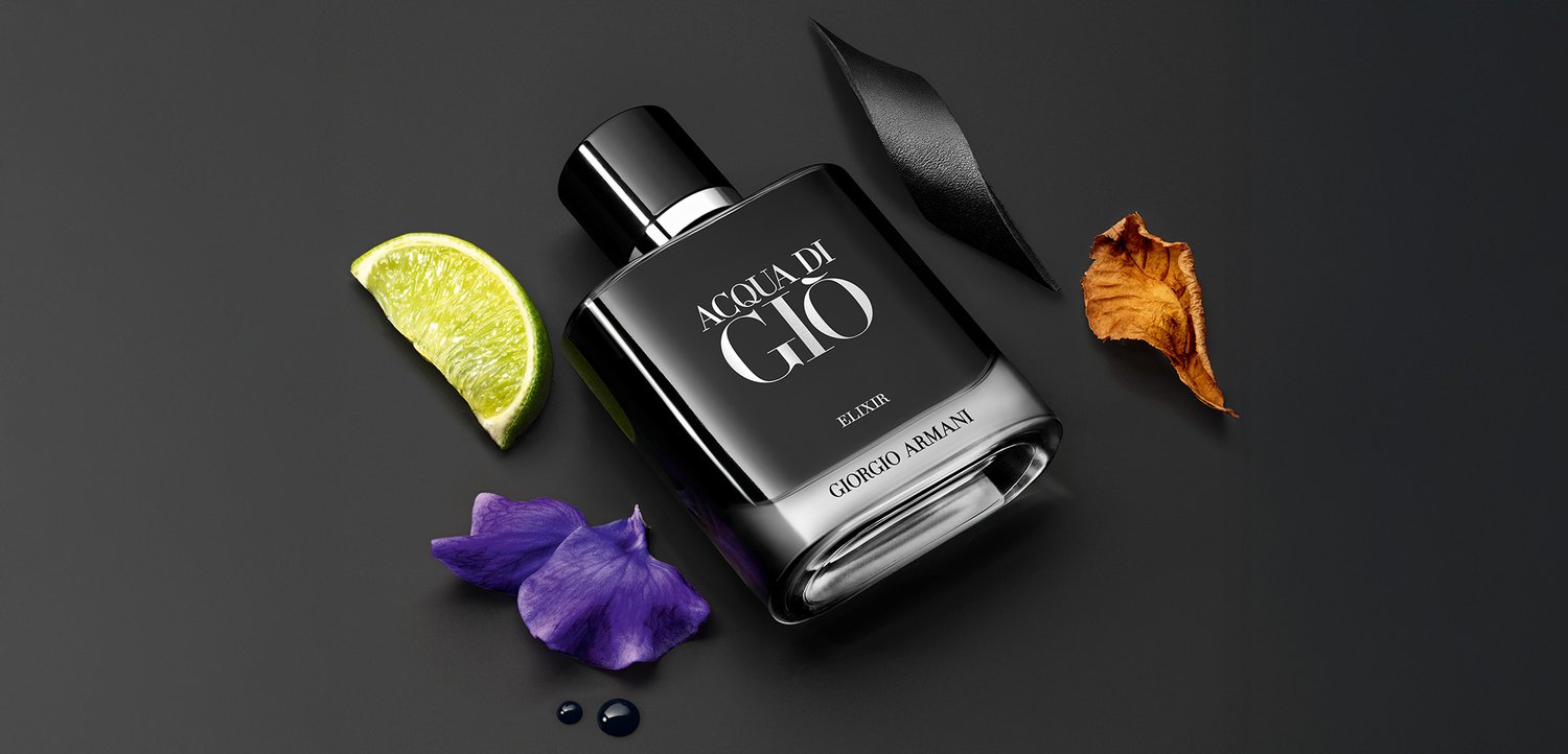 Giorgio Armani Acqua di Gio Elixir, a black glass bottle with a silver cap, accompanied by a lime slice, purple petal, and dried leaf.