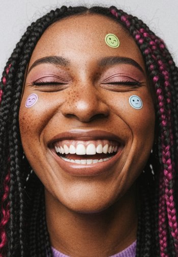 Smiling face with braided hair featuring pink highlights. Stickers in various colors placed on cheeks. Wearing a purple sweater.
