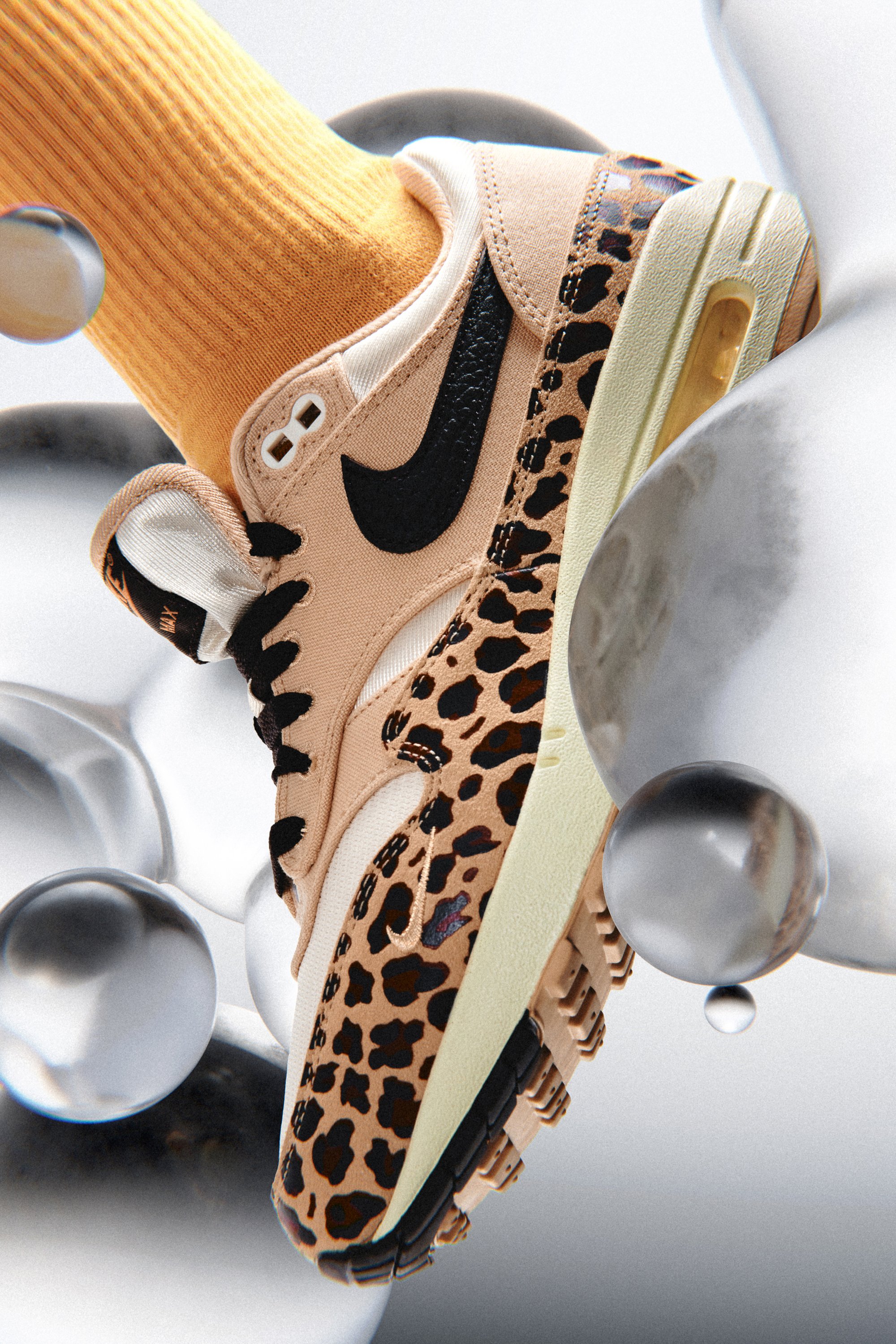 Een close-up van een Nike-sneaker met een luipaardprintontwerp, gecombineerd met een feloranje sok, tegen een grijze achtergrond met bellen.