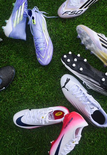Diverses chaussures de football, y compris des Adidas F50 violettes, des Puma blanches et rouges et des Nike Mercurial blanches et rouges, disposées sur de l'herbe verte avec des gouttes d'eau visibles.