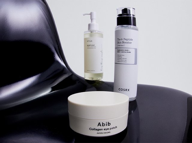 Drei Hautpflegeprodukte auf einem schwarzen Stuhl: ein Reinigungsöl, ein Peptidserum und ein Kollagen-Augenkissen, alle mit unterschiedlichen Etiketten.