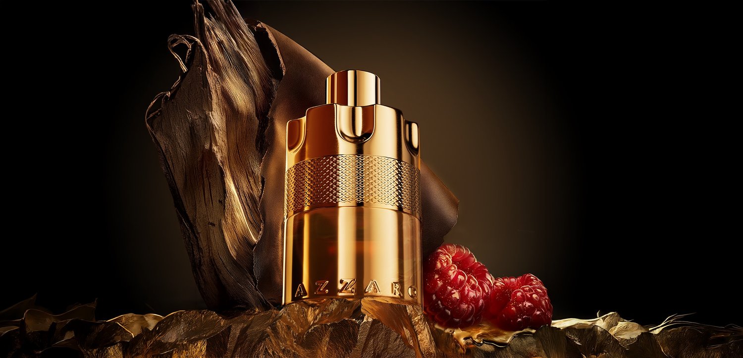 Flacon de parfum métallisé doré Azzaro posé sur des feuilles sèches avec deux framboises fraîches sur un fond sombre.