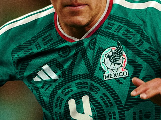 Zielona koszulka piłkarska z misternymi czarnymi wzorami, białymi paskami Adidas i haftowanym emblematem reprezentacji Meksyku.