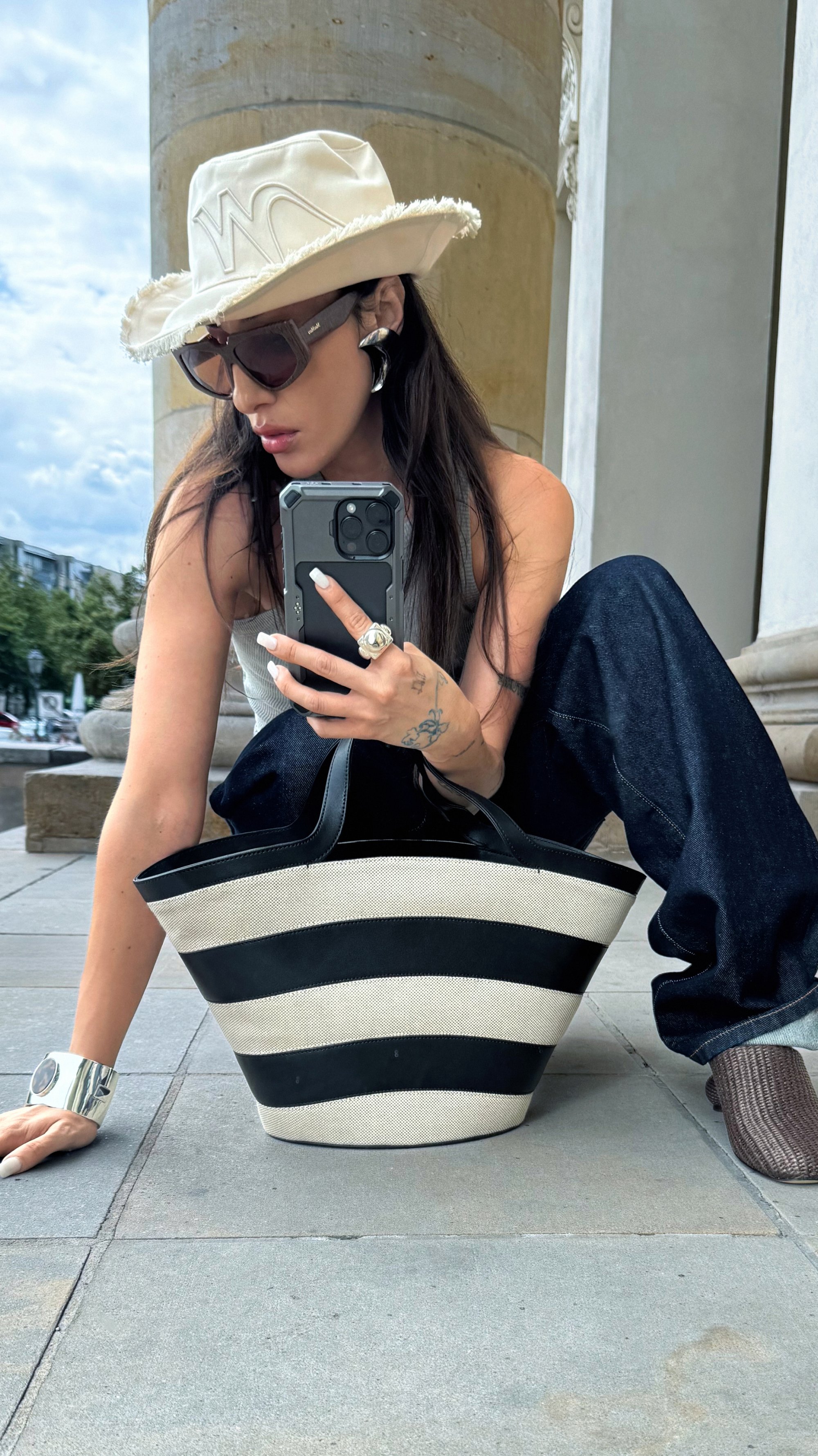 Borsa a spalla a strisce nere e crema con texture in tessuto, caratterizzata da robuste maniglie nere. Indossata con pantaloni in denim scuri e una maglietta chiara.