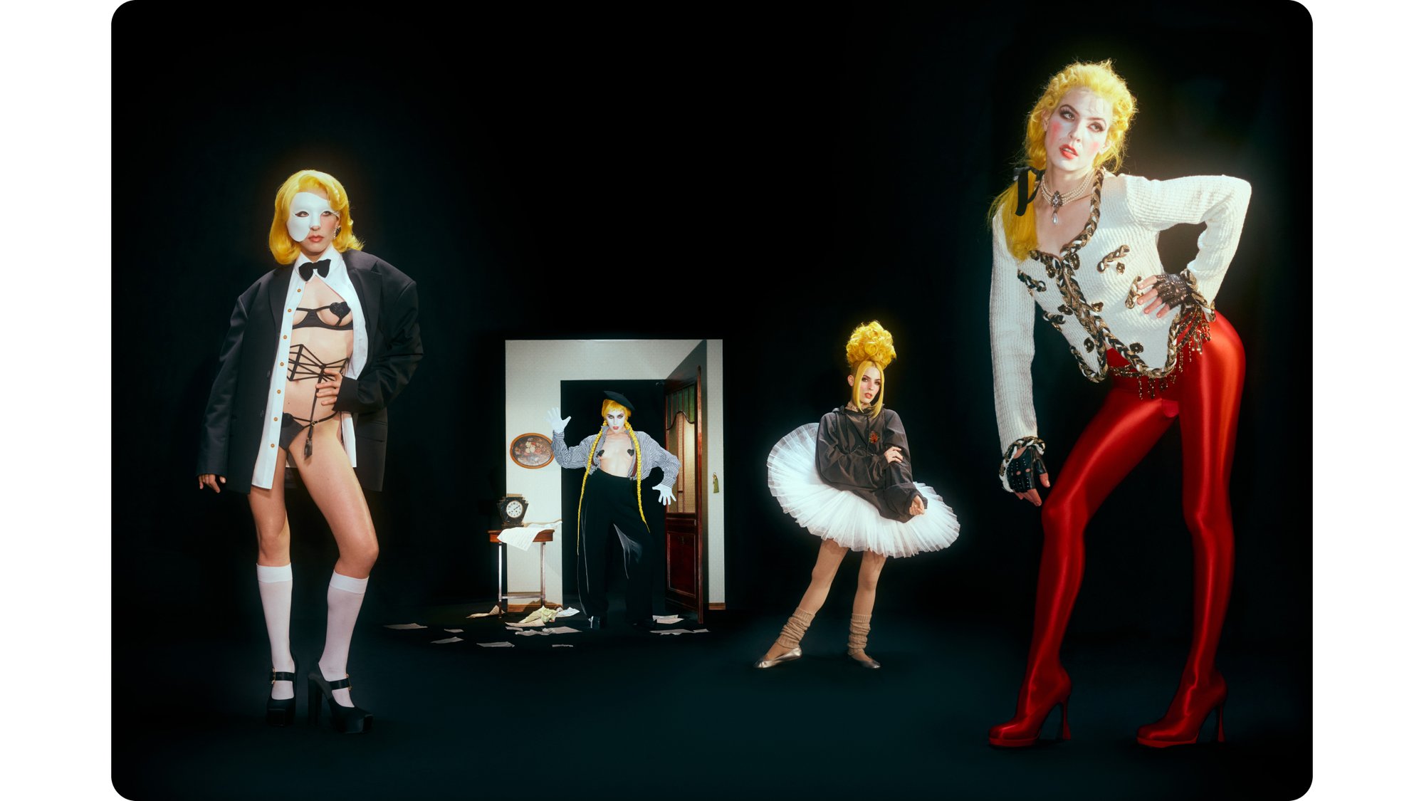 Four individuals in striking outfits pose dramatically: one wears a tuxedo with lingerie, another dons a tutu, while the others showcase unique styles. A doorframe reveals a disheveled room.