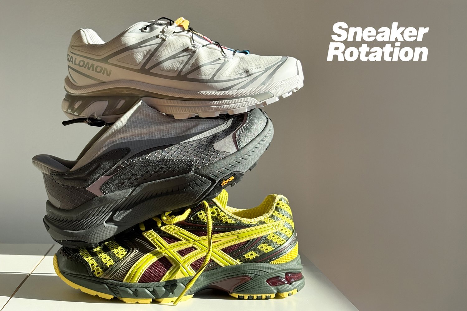 Drie paar sportschoenen verticaal gestapeld op een heldere ondergrond, met de tekst "Sneaker Rotatie" weergegeven aan de rechterkant.