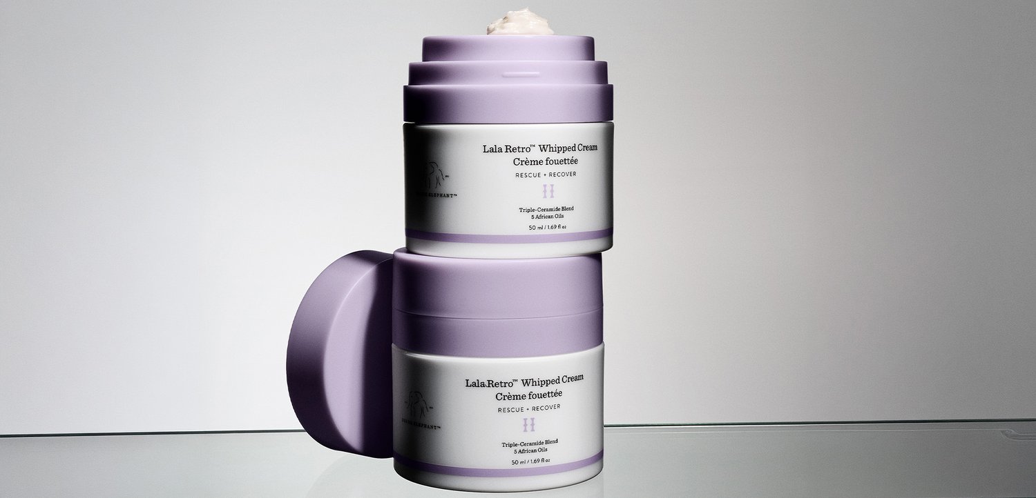 Zwei übereinandergestapelte helllila Tiegel des Lala Retro Whipped Cream Moisturizers, einer davon mit abgenommenem Deckel und einer kleinen Menge Creme oben sichtbar.