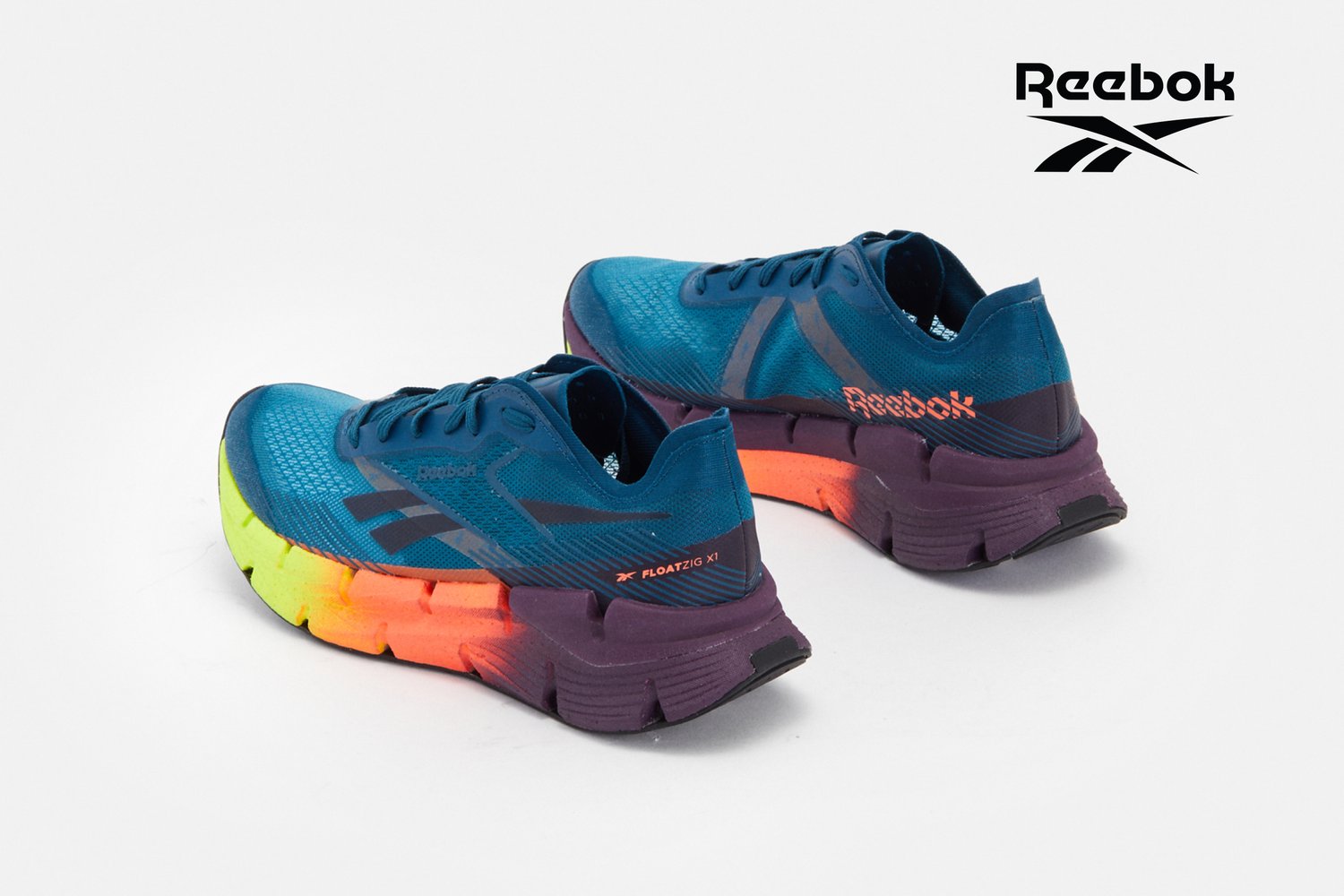 Zapatillas deportivas azules con una suela de degradado colorido que muestra amarillo, naranja y púrpura, destacadas con un prominente logo de Reebok.