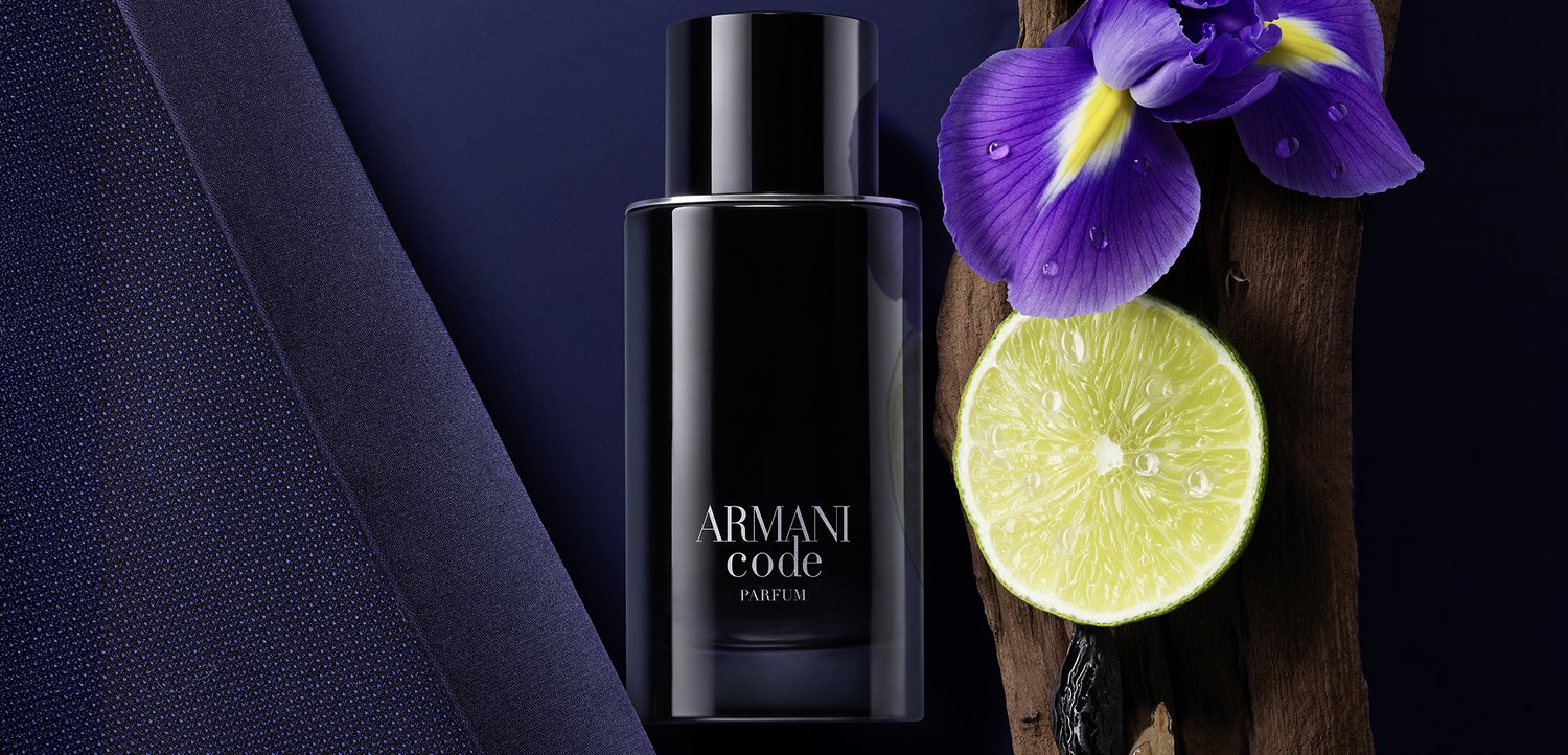 Black Armani Code perfume bottle beside a purple iris flower, lime half, and dark wood on a navy blue background.