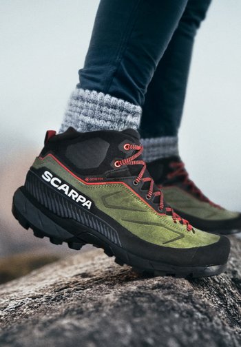 Le scarpe da trekking Scarpa presentano una combinazione di colori verde e nero, materiali in suede e sintetici, e accenti rossi. La suola è robusta e dotata di profili profondi.
