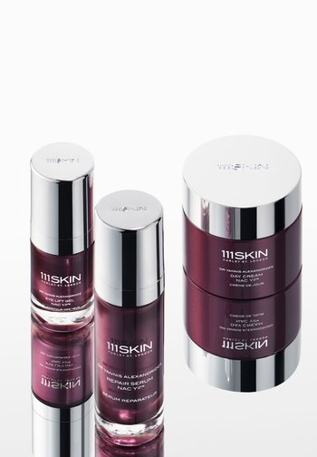 Trzy produkty do pielęgnacji skóry 111Skin z ciemnofioletowymi opakowaniami i błyszczącymi srebrnymi nakrętkami na powierzchni odbijającej światło, oznaczone jako żel do liftingu oczu, serum naprawcze i krem na dzień.