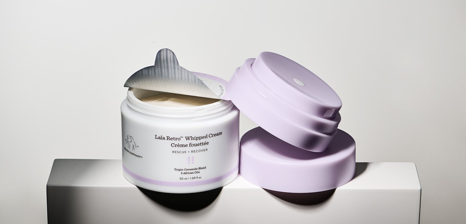 Geöffneter Tiegel Lala Retro Whipped Cream Feuchtigkeitscreme mit abgenommenem Deckel und zurückgezogener Folienversiegelung, steht auf einer weißen Oberfläche im hellen Licht.