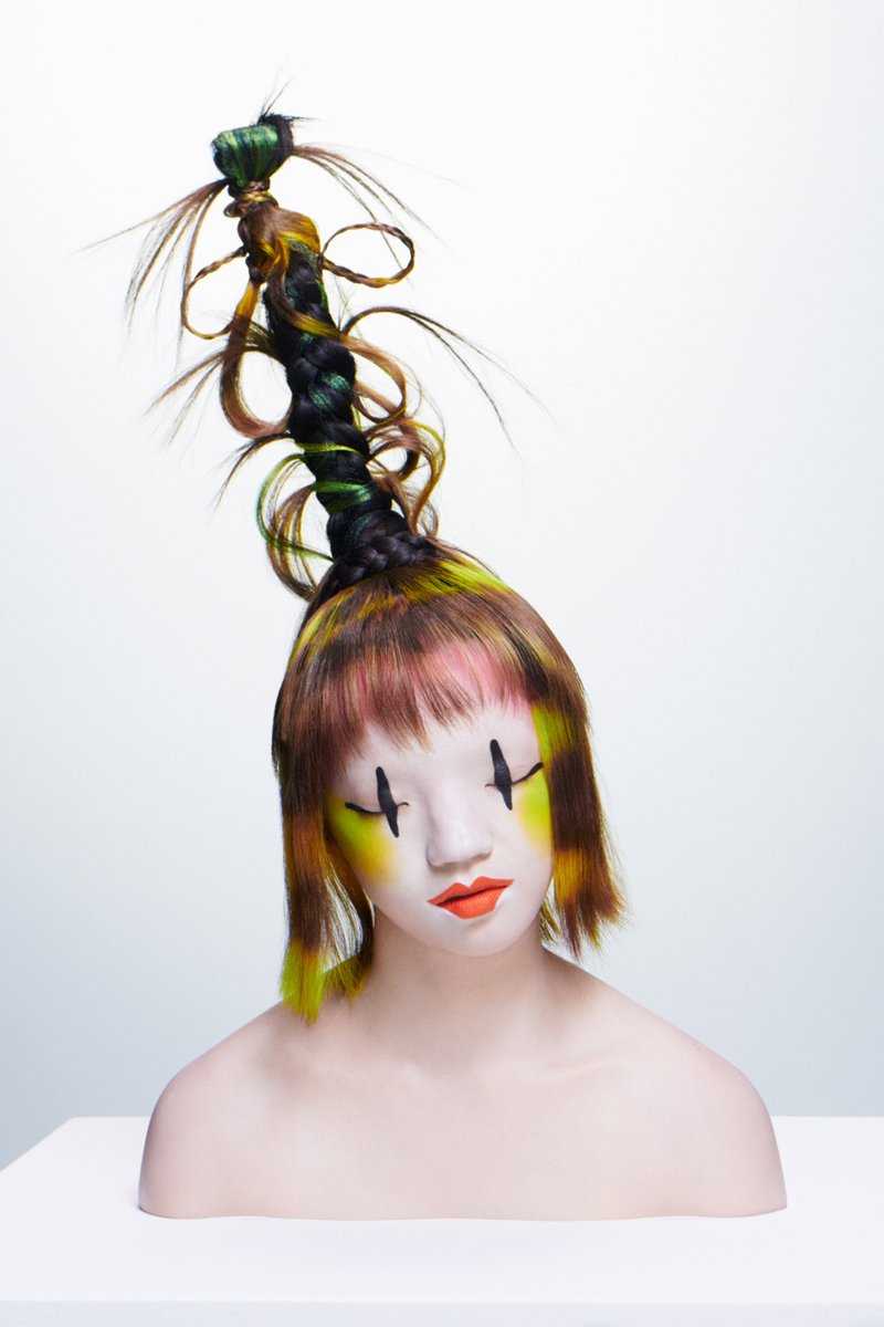 A stylized mannequin with striking, colorful hair in an elaborate braid, featuring bold makeup and a smooth, expressionless face.