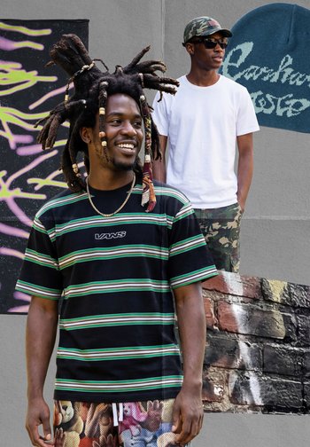 Twee jonge mannen staan tegen een graffiti-muur, de ene met lange dreadlocks en een gestreept Vans-shirt, de andere met een zonnebril, een wit T-shirt en camouflagebroek.