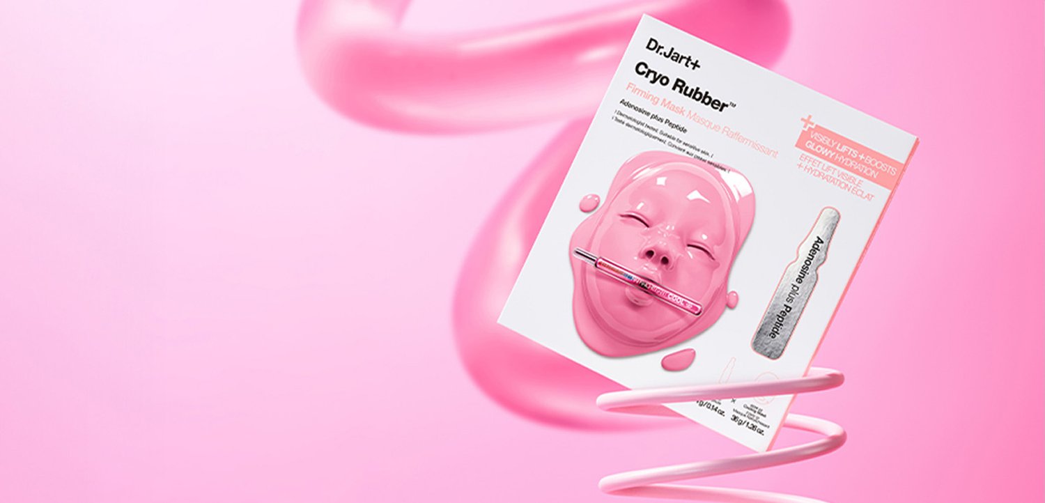 Innpakning av Dr. Jart+ Cryo Rubber Firming Mask med en blank rosa ansiktsmaske og påføringsskje på en rosa bakgrunn.