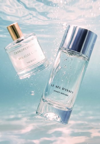 Two clear glass perfume bottles labeled Zarkoperfume Molecule C-19 and Le Sel D’Issey by Issey Miyake submerged underwater with bubbles.