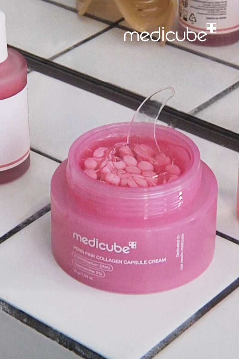 Barattolo rosa aperto di Medicube Collagen Capsule Cream con piccole capsule rosa e spatola trasparente all’interno su superficie piastrellata.