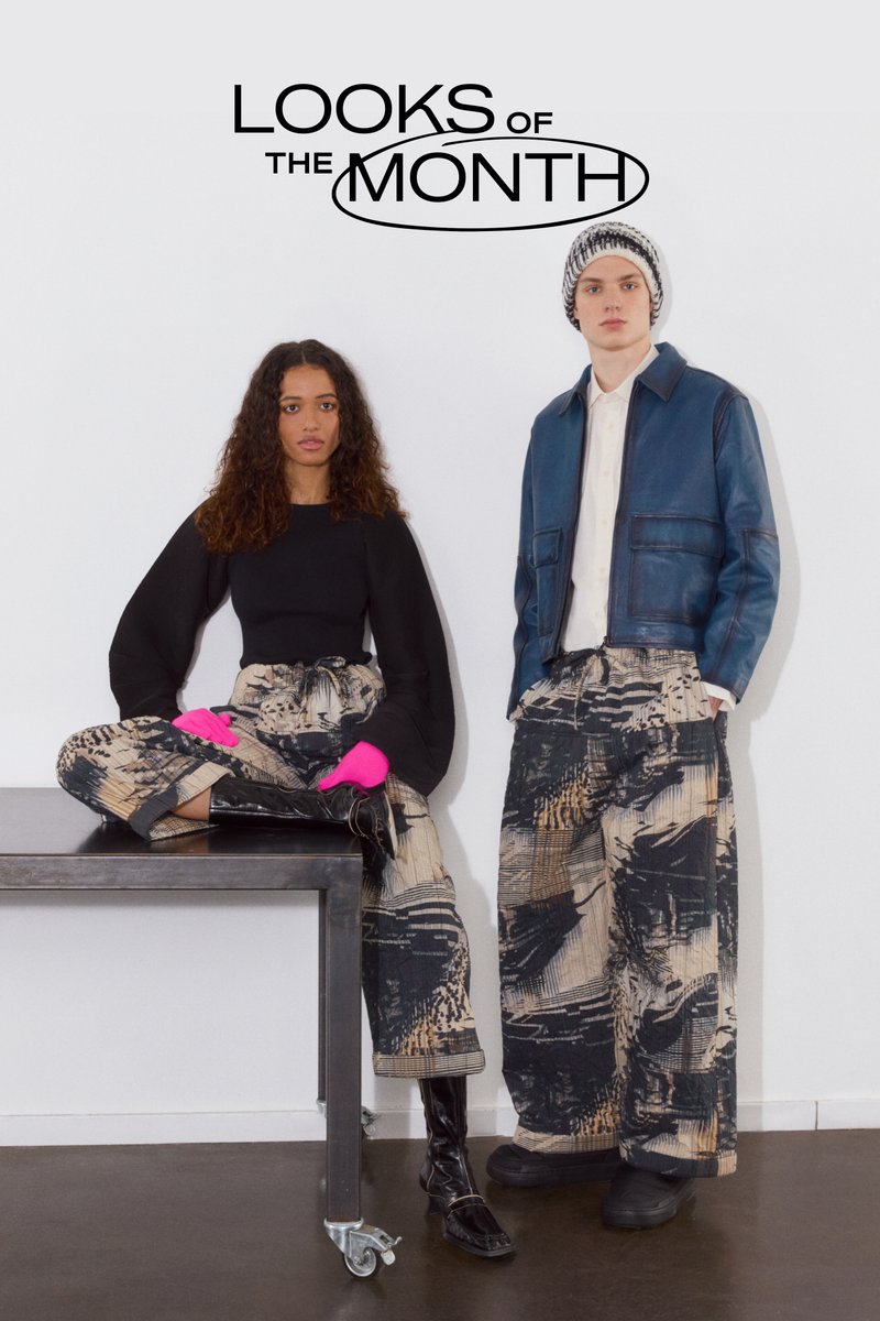 Two models stand against a white wall; one sits on a table wearing a black top and bold pink gloves, the other in a blue jacket and patterned pants.