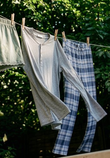Camisa gris de manga larga, pantalones de pijama azules a cuadros y pantalones cortos colgados en un tendedero con pinzas de madera al aire libre.