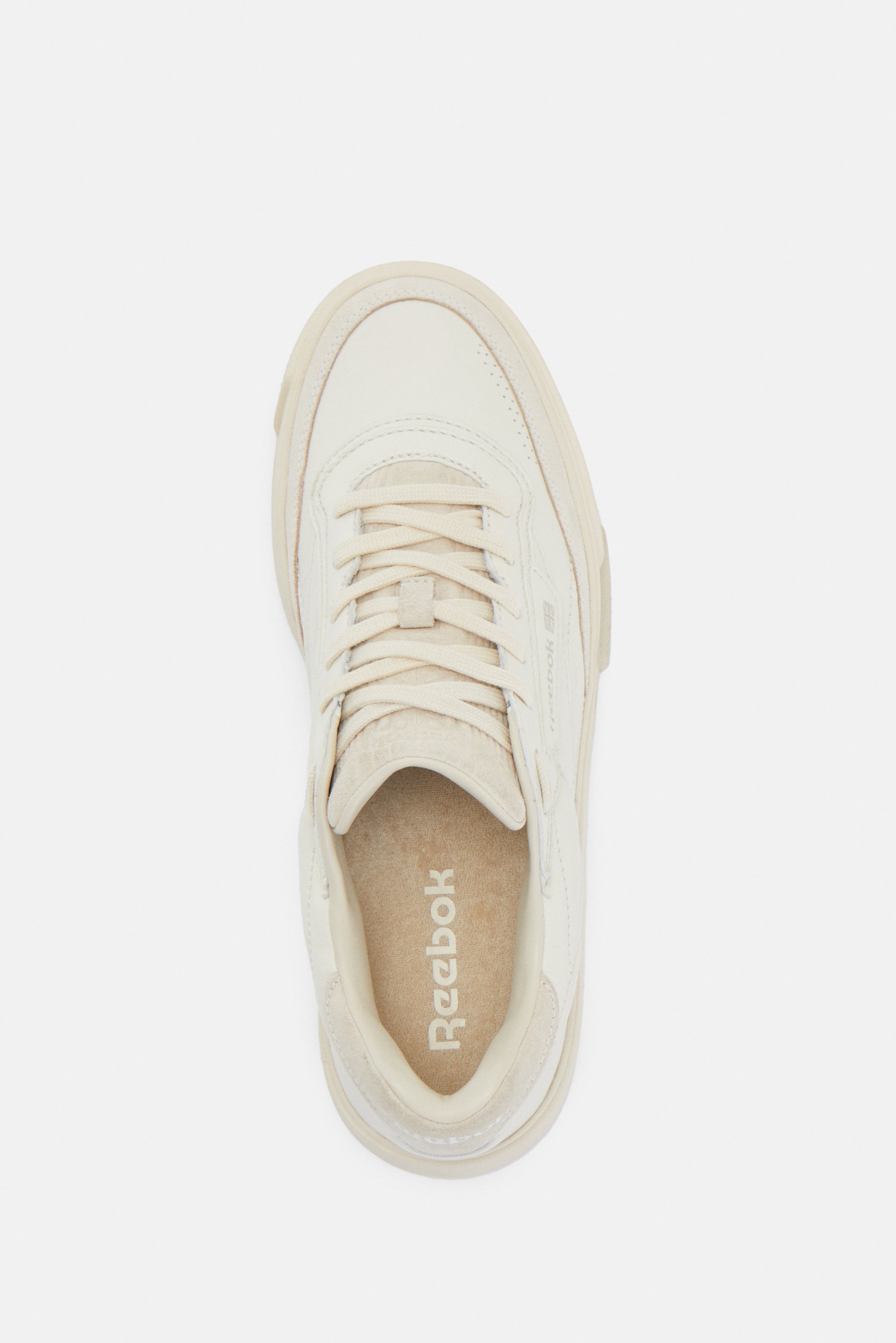 Zapatilla Reebok de color crema, con cordones, paneles texturizados y logo en la plantilla, mostrada desde una vista superior.