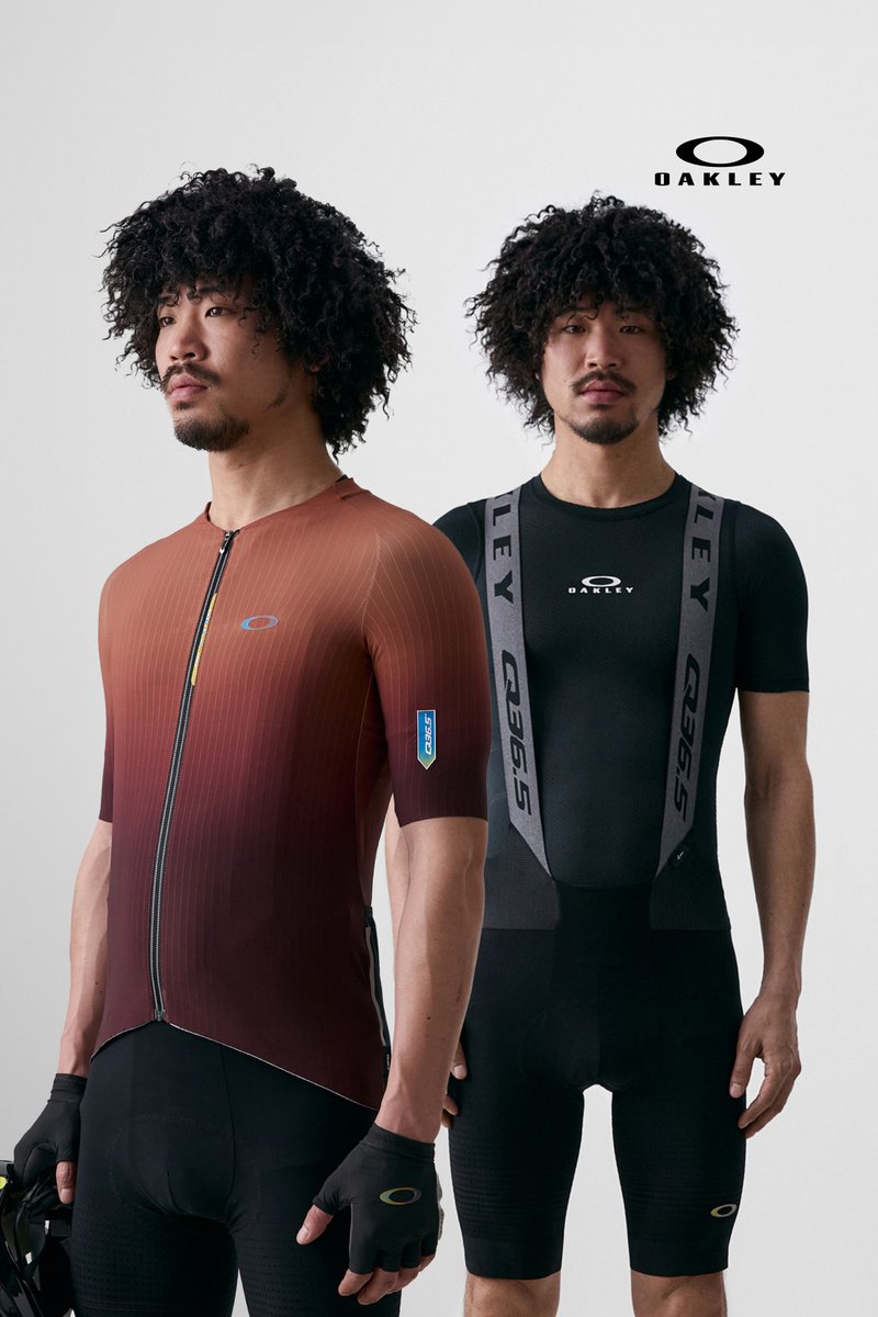 Twee mannen met krullend haar poseren in fietsoutfits, de ene draagt een rode gradient jersey en de andere een zwarte bibshort, beide voorzien van Oakley-logo's.