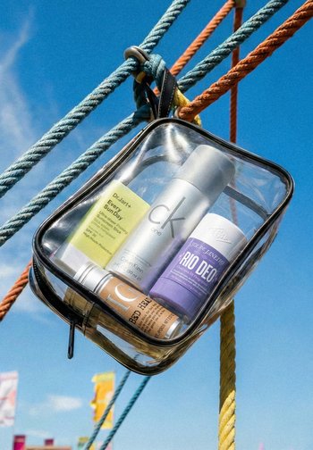 Klare Kulturtasche, die an bunten Seilen hängt und Sonnenschutz, Deodorant und Körperspray vor blauem Himmel enthält.