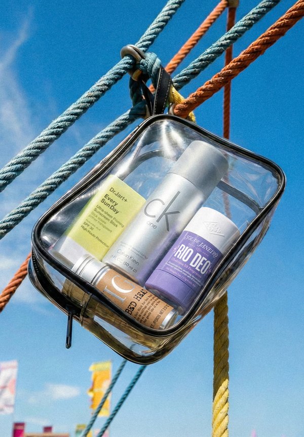 Klare Kulturtasche, die an bunten Seilen hängt und Sonnenschutz, Deo und Körperspray vor blauem Himmel enthält.