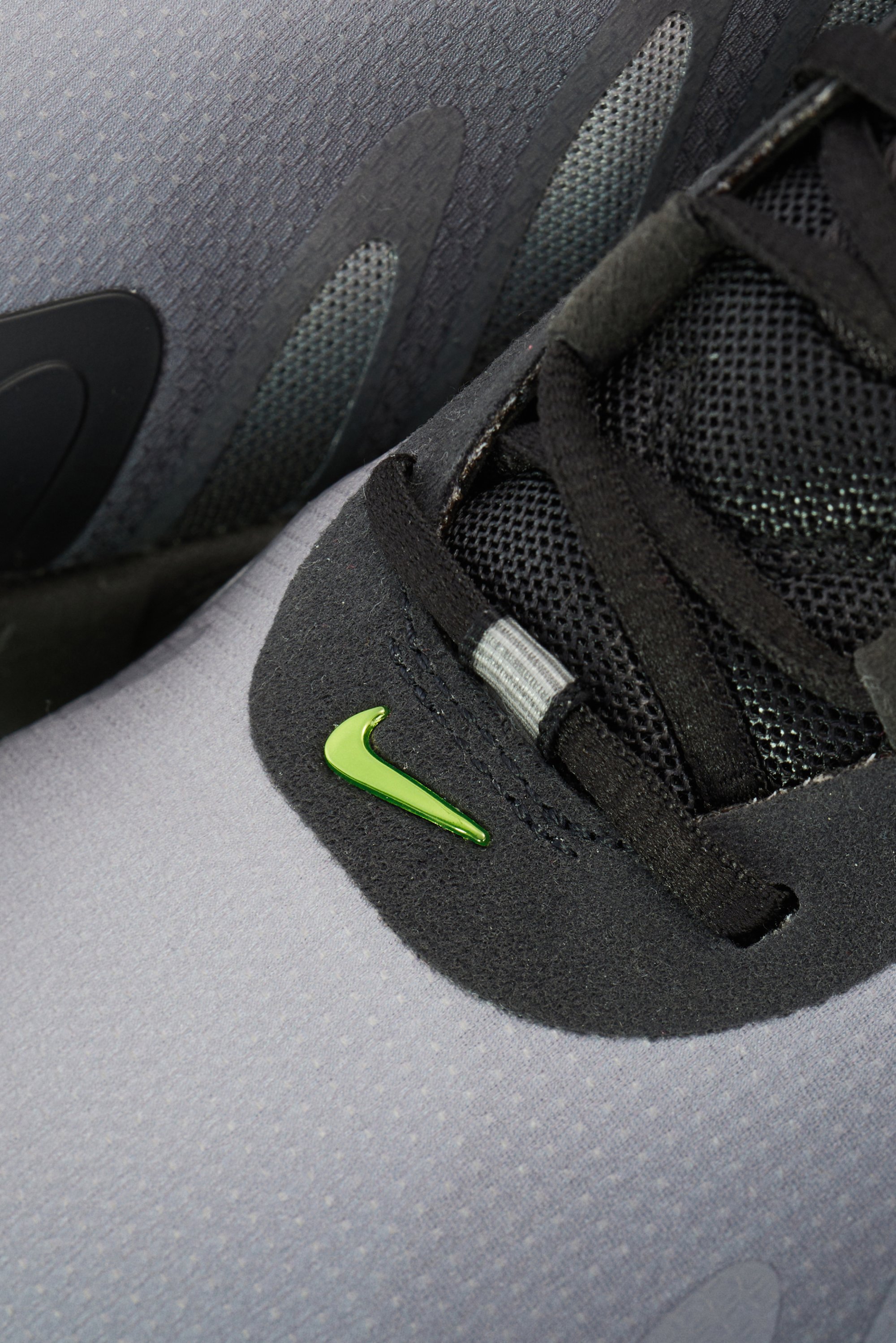 Close-up view of a gray Nike sneaker featuring a black mesh upper and a bright green swoosh logo on the side.