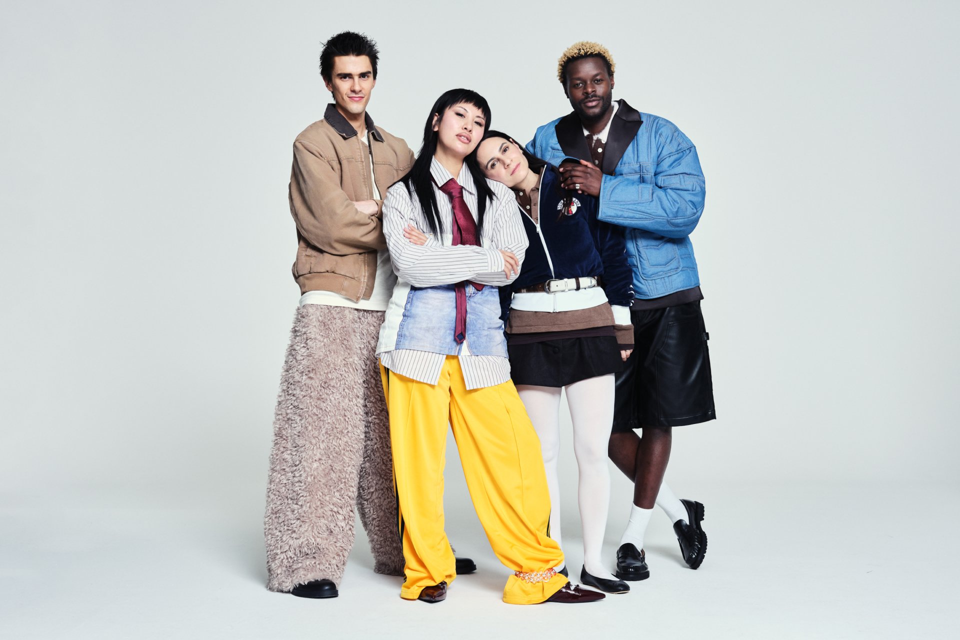 Quattro persone diverse posano insieme, mostrando outfit unici e alla moda su uno sfondo neutro, irradiano fiducia e solidarietà.