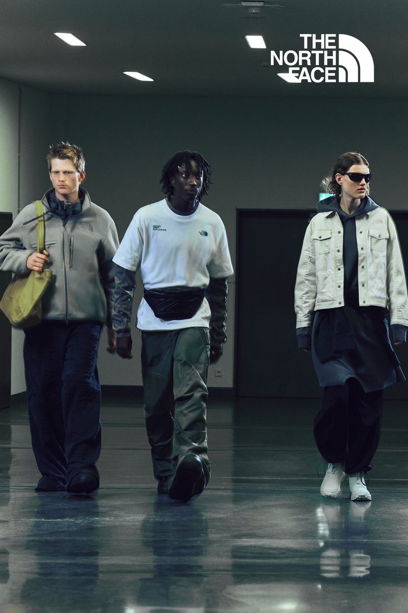 Tre modelli camminano attraverso un corridoio moderno, indossando abbigliamento casual e alla moda di The North Face. L'ambientazione è caratterizzata da luci brillanti e pavimenti eleganti.