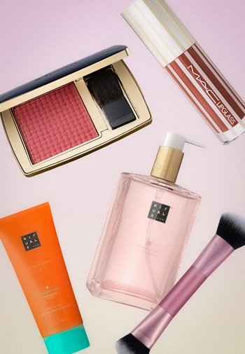 Estée Lauder roze blush met kwastje, MAC lipgloss, Rituals aftersuncrème, Rituals handzeep en dubbelzijdige make-up kwast op een roze achtergrond.