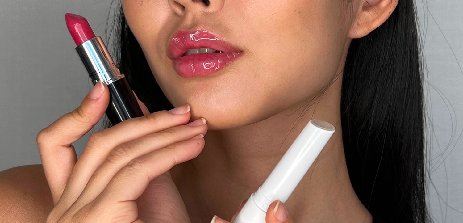 Rossetto con custodia nera e tonalità rosa nella mano sinistra, lucidalabbra in tubo bianco nella mano destra; texture liscia che mette in risalto le labbra.