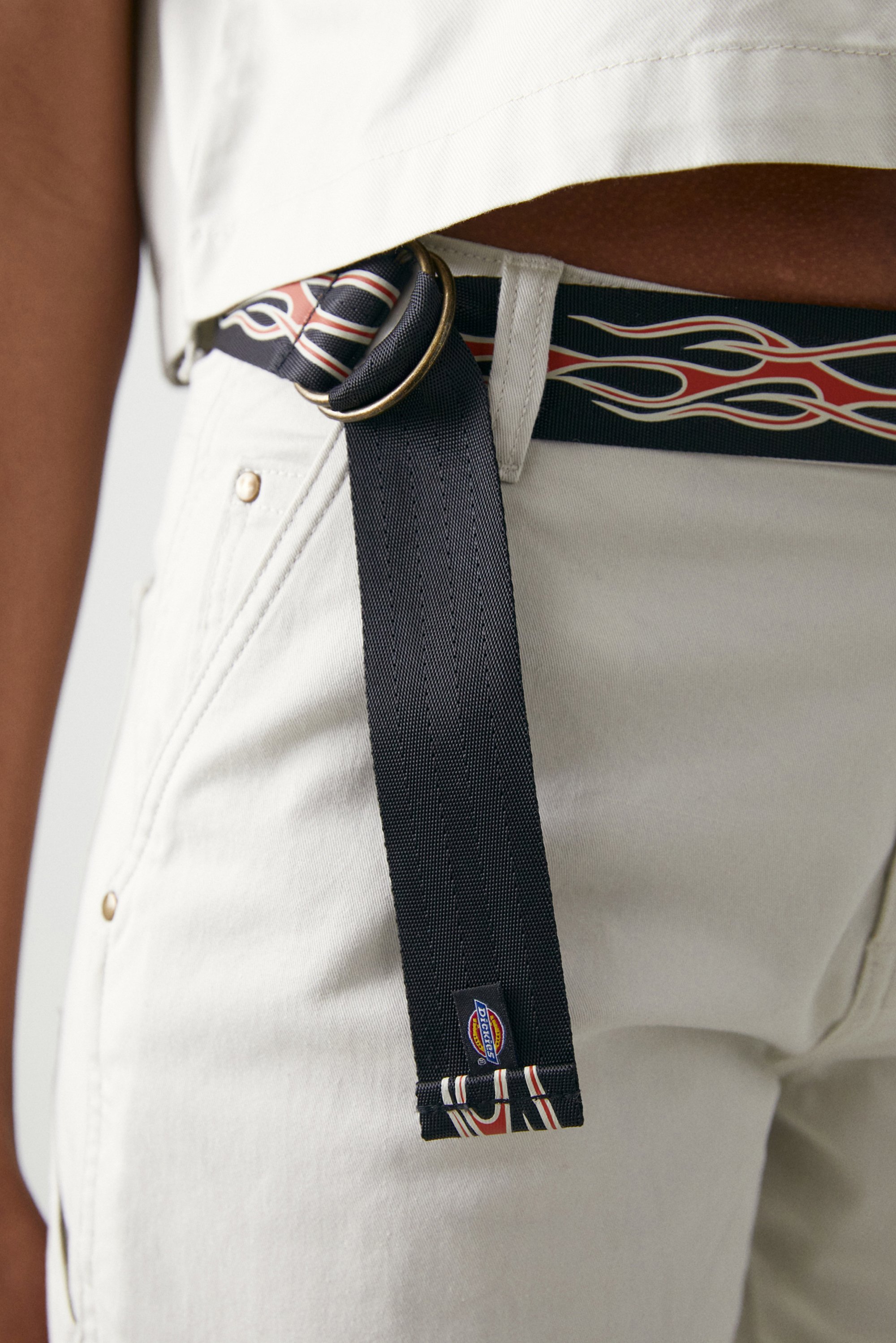 Close-up of a person's waist wearing light-colored pants and a distinctive black belt with red and white flame designs and a metal buckle.
