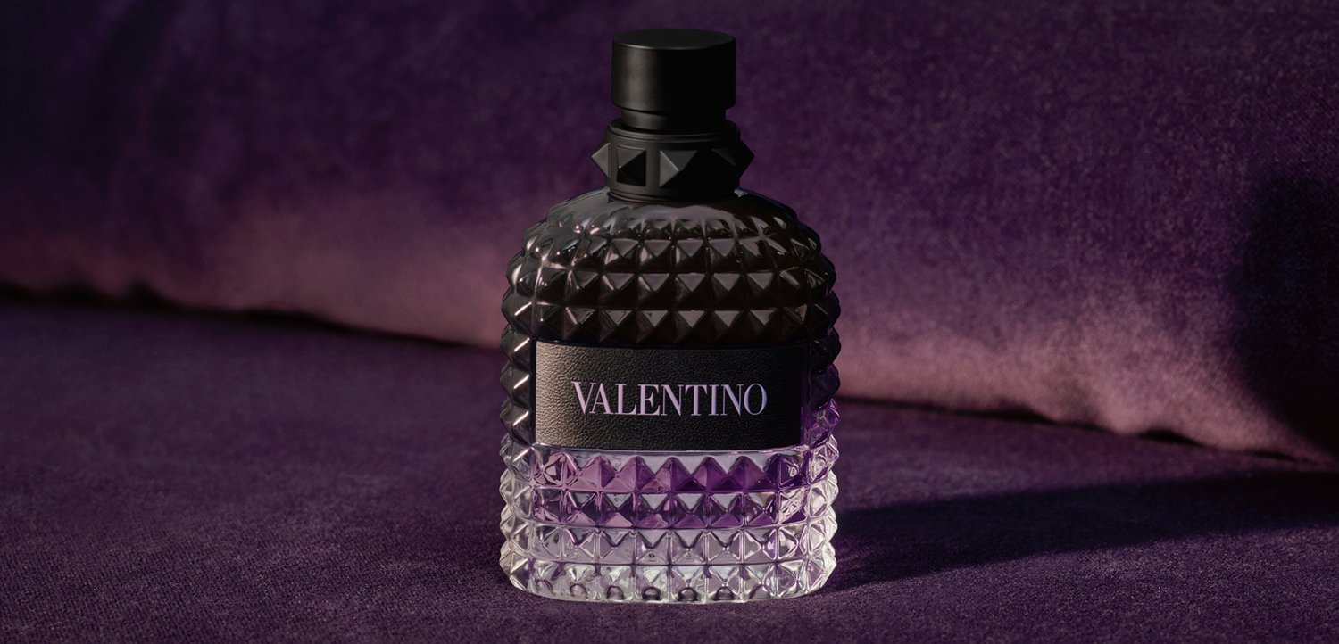 Black and clear studded glass Valentino perfume bottle with black cap on purple velvet surface and background.