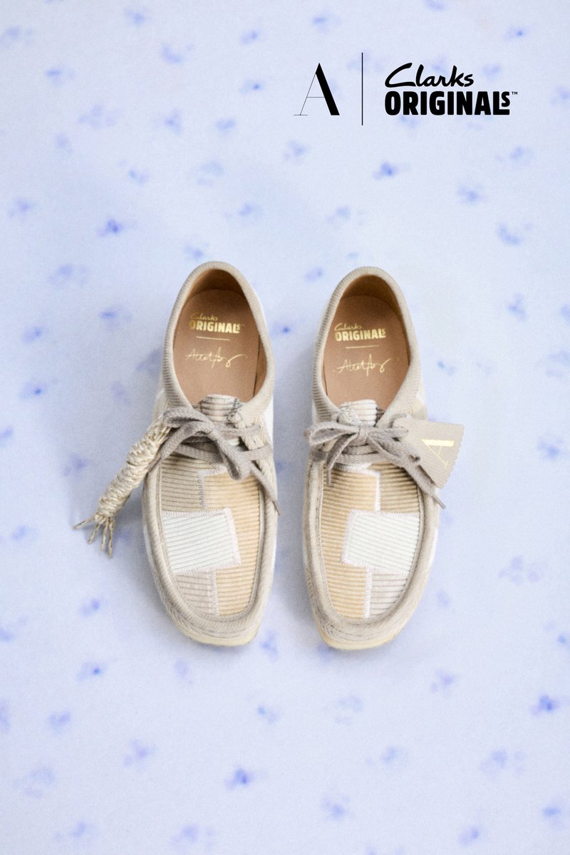 Beige Clarks Originals Loafers mit Patchwork-Design und geflochtener Schnürdetail am linken Schuh, dargestellt auf einem hellblauen gesprenkelten Hintergrund.