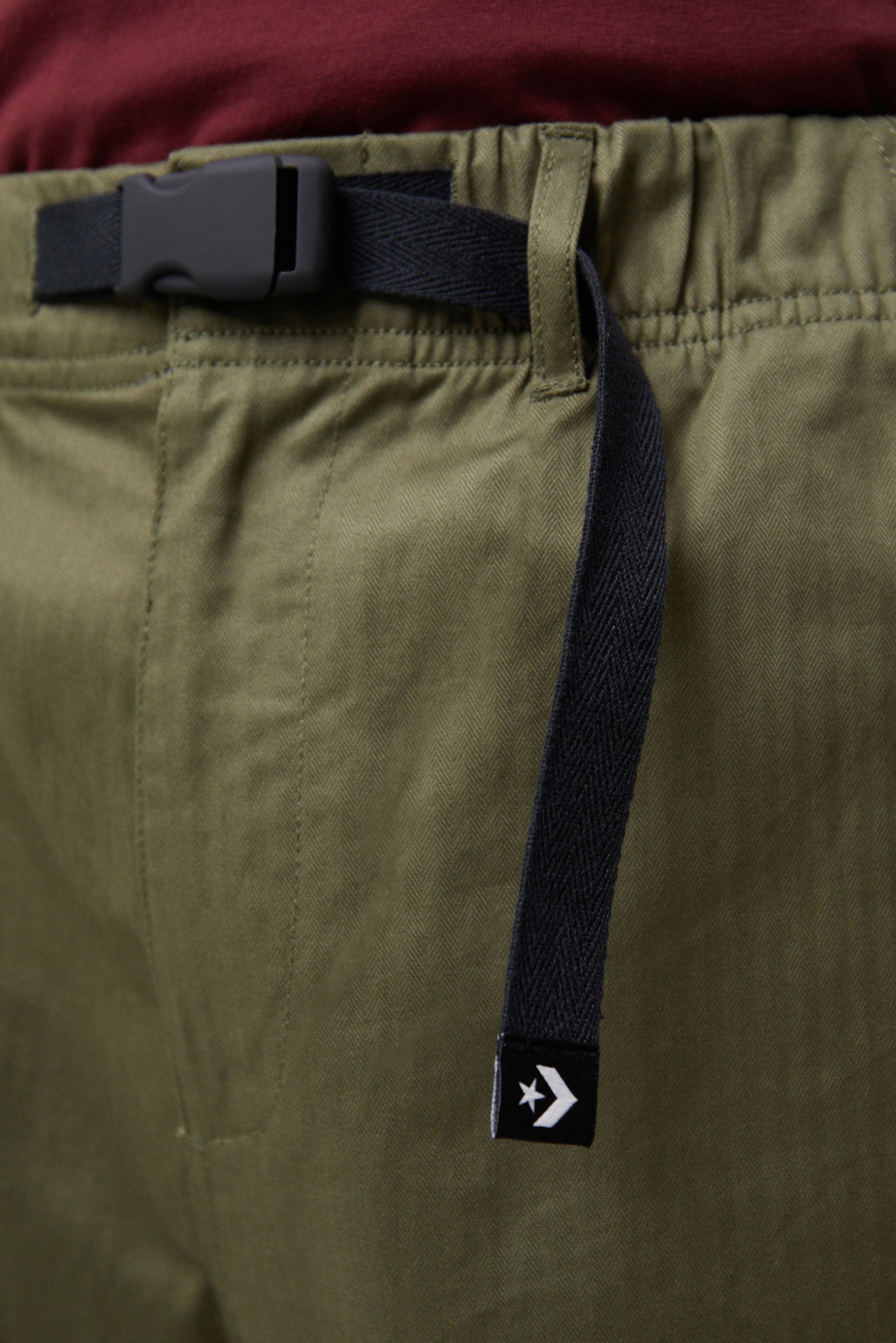 Close-up of olive green pants with an elastic waist and a black belt loop. A small label with a star logo is visible on the side.