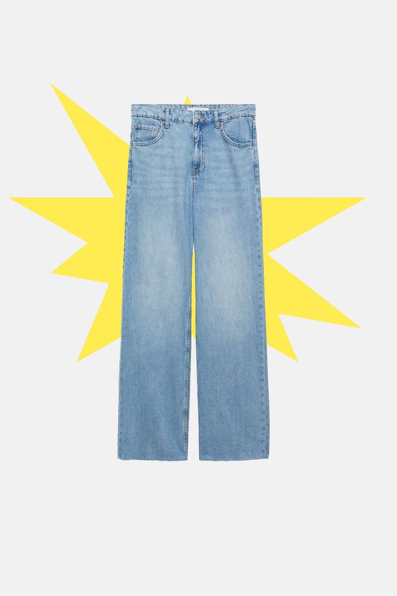 Jeans din denim de culoare albastru deschis, cu picioare largi, dotate cu buzunare frontale, nasture și fermoar, prezentate așezate plat pe un fundal alb, cu o explozie galbenă în spate.