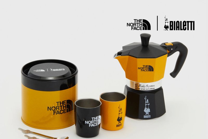 Cafetera Bialetti Moka Express en color naranja y negro con forma octagonal; incluye dos tazas a juego y un tarro de almacenamiento redondo.