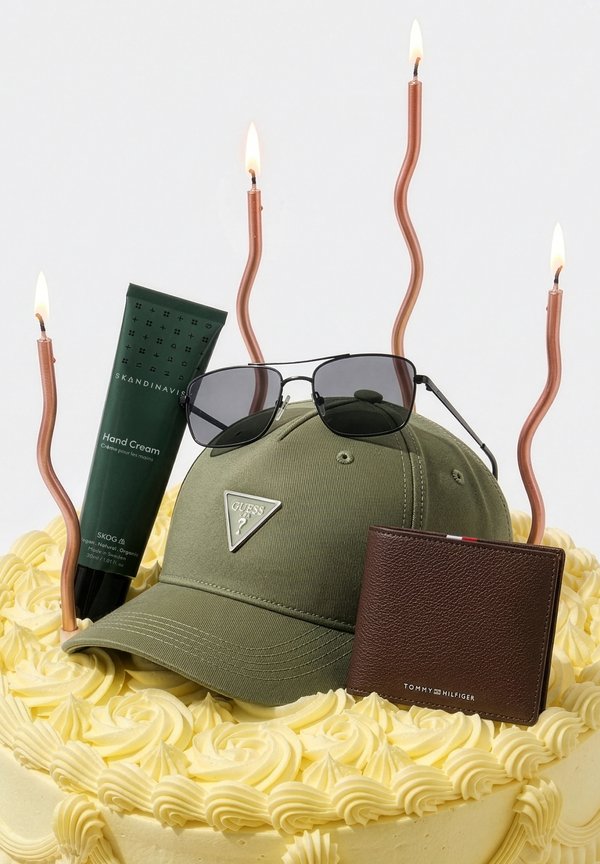 Gelber Glasurkuchen mit einem grünen Guess-Cap, schwarzen Sonnenbrillen, braunem Tommy Hilfiger Portemonnaie, grüner Skandinavisk Handcreme und vier brennenden, verdrehten Kerzen darauf.