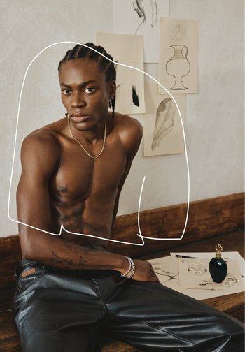 Model met gevlochten haar poseert zonder shirt, met een gouden ketting. Zwarte leren broek met een logo, omringd door kunstschetsen en een parfumflesje.