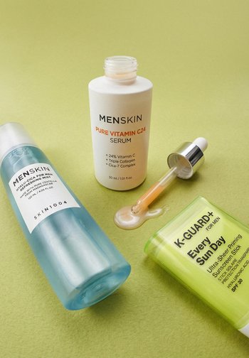 Tre hudplejeprodukter til mænd på grøn overflade: blå fugtgivende mist, hvid C-vitaminserum med pipette og grøn solcremeklip.